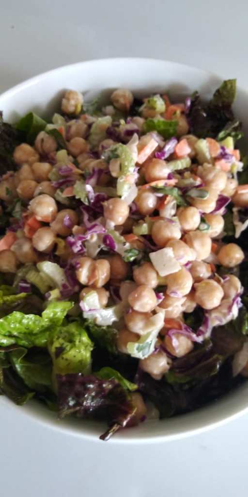 A bowl of chickpea salad with mixed greens, purple cabbage, diced vegetables, and a creamy dressing.